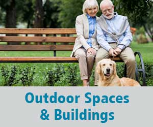 Thumbnail image for Outdoor Spaces & Buildings domain. Image is of an older woman and an older man sitting close together on a park bench with a dog in front of them.