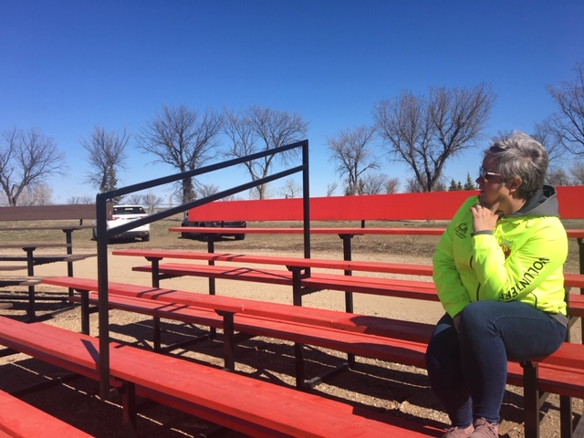 Image of bleacher in Rosetown with hand railings that Age-Friendly Rosetown ensured were installed. A woman volunteer is sitting on the bleacher, looking into the distance.