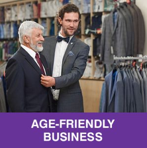 Thumbnail photo of well-dressed young man in clothing store fitting older man with new suit. Caption is Age-Friendly Business