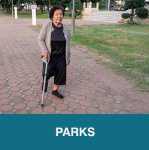 Thumbnail image of older Asian woman using a cane, walking on a large sidewalk in a park. Caption is Parks.