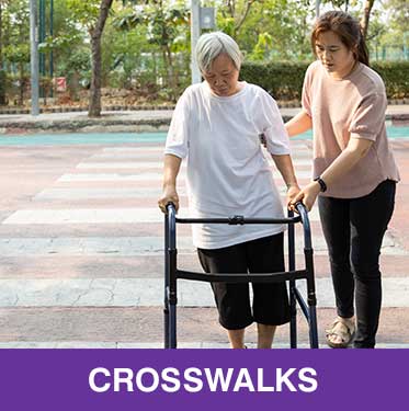 Thumbnail image of older Asian woman using a walker, with younger Asian woman assisting her. They are crossing a street crosswalk. Caption is Crosswalks.